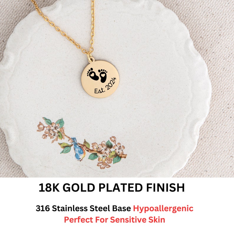 May include: Gold plated necklace with a round pendant featuring a footprint design and the text "Est. 2024".
