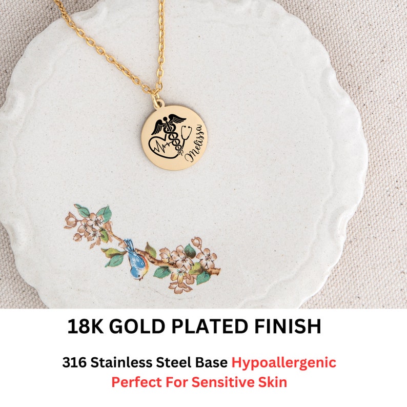 May include: Gold plated necklace with a round pendant featuring a medical symbol, a heart, and the name "Melissa". The pendant is on a white plate with a floral design. 18K Gold Plated Finish. 316 Stainless Steel Base Hypoallergenic. Perfect For Sensitive Skin.