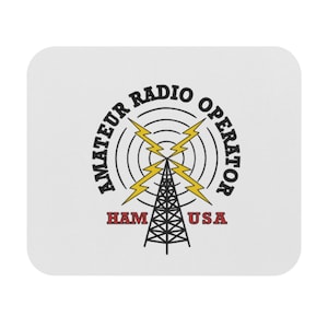 Peut inclure: Sous-verre carré blanc aux coins arrondis. Le motif présente une tour radio noire, des éclairs jaunes et des cercles concentriques. Le texte comprend "AMATEUR RADIO OPERATOR" et "HAM USA" en noir et rouge.