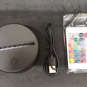 May include: A black round base with a slot for a light panel, a USB cable, and a white remote control with buttons for on, off, and various color options.