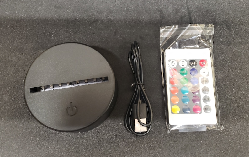 May include: A black round base with a slot for a light panel, a USB cable, and a white remote control with buttons for on, off, and various color options.