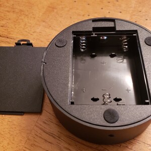 May include: A black plastic battery compartment with a removable cover. The compartment has two sets of spring-loaded terminals for inserting batteries.