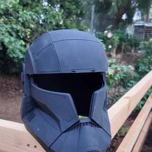 May include: A black plastic helmet with a detailed design. The helmet has a visor and a textured surface.