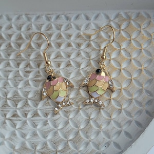 May include: A pair of gold fish-shaped earrings with pink, yellow, and green enamel and clear rhinestones.