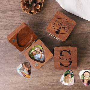 Könnte beinhalten: Zwei Holzkisten mit gravierten Namen und Gitarren-Plektrum-Designs. Jede Kiste enthält ein Gitarren-Plektrum mit einem darauf gedruckten Foto. Die Kisten befinden sich auf einer Holzoberfläche.