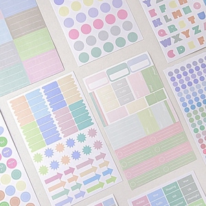 Könnte beinhalten: Ein Set mit pastellfarbenen Planer-Stickern mit verschiedenen Designs, darunter Kreise, Sterne, Pfeile und Etiketten. Die Sticker sind perfekt, um Ihrem Planer einen Hauch von Farbe und Organisation zu verleihen.