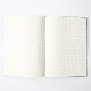 May include: An open notebook with a white cover and gridded pages. The notebook is lying flat on a white surface.
