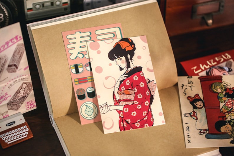 K&ouml;nnte beinhalten: Zwei Vintage-Postkarten mit japanischen Illustrationen. Die erste Postkarte zeigt eine Frau in einem roten Kimono mit wei&szlig;en Blumen, und die zweite Postkarte zeigt einen roten Briefkasten mit einem M&auml;dchen in einem wei&szlig;en Kleid und einer roten Schleife.