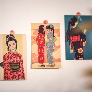 K&ouml;nnte beinhalten: Drei gerahmte Illustrationen von Frauen in traditioneller japanischer Kleidung, bekannt als Kimonos. Die Kimonos sind in verschiedenen Farben und Mustern, darunter Rot, Blau und Schwarz. Die Illustrationen sind auf einem cremefarbenen Hintergrund gedruckt.
