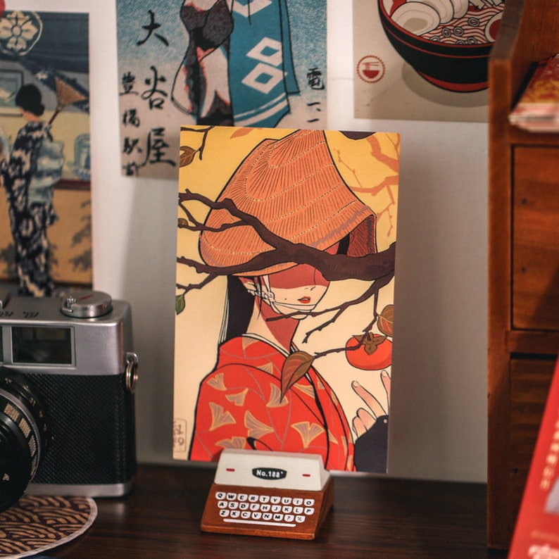 K&ouml;nnte beinhalten: Eine Postkarte im Vintage-Stil mit einer Frau, die einen traditionellen japanischen Hut und einen Kimono tr&auml;gt. Die Frau steht vor einem Kaki-Baum mit einer reifen Kaki-Frucht. Die Postkarte hat einen gelben Hintergrund mit einem braunen Ast und Bl&auml;ttern. Der Text "No. 128" ist in der rechten unteren Ecke gedruckt.