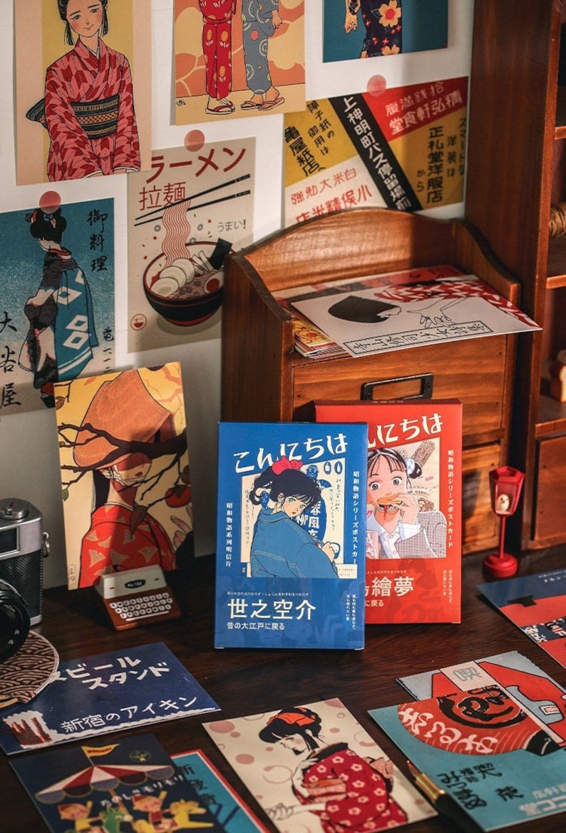K&ouml;nnte beinhalten: Eine Sammlung von Vintage-Postkarten aus Japan mit Illustrationen von Menschen, Essen und traditionellen japanischen Designs. Die Postkarten werden auf einem Holzregal und einem Holztisch ausgestellt. Der Text auf den Postkarten lautet "Ramen", "拉麵", "世之空介", "繪夢", und "こんにちは".
