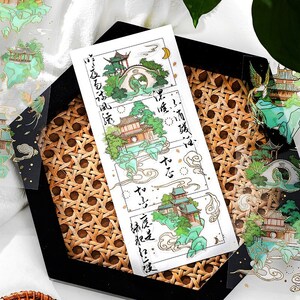 Pu&ograve; includere: Un foglio di adesivi trasparenti con un design da giardino cinese tradizionale. Gli adesivi sono in uno schema di colori verde e oro e includono testo in caratteri cinesi.