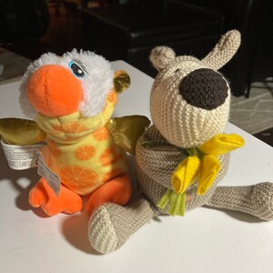 May include: Two plush toys, one is a yellow and orange bird with a white fluffy head and the other is a brown knitted dog holding yellow flowers.