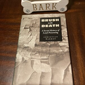 May include: A book titled "Brush with Death: A Social History of Lead Poisoning" by Christian Warren. The book cover features a textured, gray and white design.