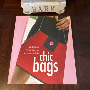 May include: A book titled "chic bags" with a pink cover and a red handbag on the front. The book title is in white text and the subtitle is "22 Handbags, Purses, Totes, and Accessories to Make".