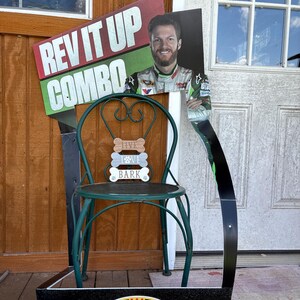 May include: A promotional display featuring a green metal chair with a round seat. Above the chair is a sign that reads "REV IT UP COMBO" and a picture of a man. The display also includes the Bojangles' logo.