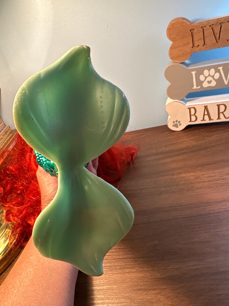 May include: A light green, abstract sculpture with a smooth, glossy finish. The sculpture has a unique, biomorphic shape, with a narrow waist connecting two larger, rounded forms. The background includes a wooden sign with the words "LIVE LOVE BAR" and a paw print.