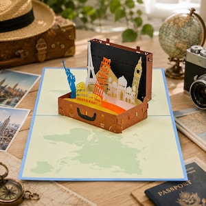 Könnte beinhalten: Eine Pop-up-Karte mit einem braunen Koffer mit Miniatur-Sehenswürdigkeiten wie dem Eiffelturm, dem Schiefen Turm von Pisa und Big Ben. Die Karte liegt auf einer Weltkarte, mit einem Globus und einer Kamera im Hintergrund. Ein Geschenk zum Thema Reisen.