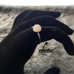 May include: A silver ring with a white round gemstone. The ring is on a black velvet surface.