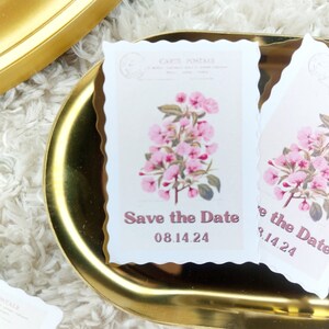 Puede incluir: Dos tarjetas blancas de guardar la fecha con ilustraciones florales rosas y el texto "Save the Date" y "08.14.24".