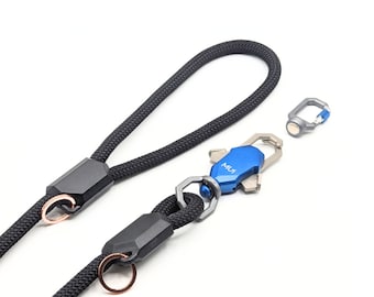 May include: A black rope dog leash with a blue and silver metal clip. The clip has the word "MUI" engraved on it. The leash has two rose gold rings.