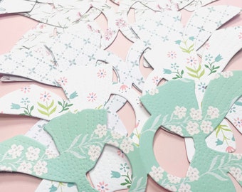 May include: A collection of paper cutouts in the shape of bows with a floral pattern. The bows are in shades of white, green, and pink.