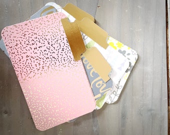 May include: A stack of colorful index cards with gold tabs. The top card has a pink and white pattern with gold glitter. The other cards have a floral pattern with gray and white accents.