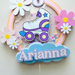 May include: A pink and white cake topper with a white roller skate, a blue cloud with the name "Arianna" and a purple number 8. The topper is decorated with white daisies and pink flowers.