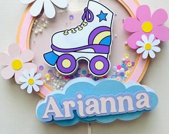 May include: A pink and white cake topper with a white roller skate, a blue cloud with the name "Arianna" and a purple number 8. The topper is decorated with white daisies and pink flowers.