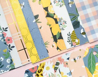 May include: A set of 15 colourful gift tags with various patterns, including floral, geometric, and lemon designs. The tags are all in the shape of a rectangle with rounded corners and have a hole punched at the top for string or ribbon.