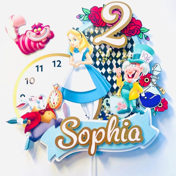 Peut inclure: Décor de gâteau sur le thème d'Alice au pays des merveilles avec une robe bleue et blanche, un lapin blanc tenant une montre de poche, le Chapelier fou et un chat du Cheshire. Le décor comprend également un numéro 2 doré et le nom "Sophia" sur une bannière bleue.