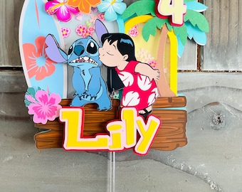 May include: A colorful cake topper featuring the characters Stitch and Lilo from the movie Lilo & Stitch. The topper includes a surfboard, flowers, a palm tree with the number 4, and the name "Lily" in yellow letters.