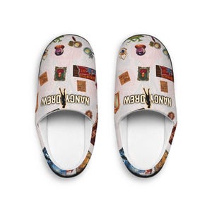 Puede incluir: Un par de zapatillas de interior blancas con un estampado colorido que incluye el texto "NANCY DREW" y varias imágenes relacionadas con la serie de libros de Nancy Drew.