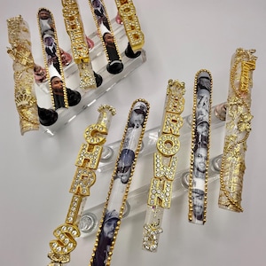 May include: A set of custom-designed acrylic nails. The nails feature portraits, gold-colored embellishments, and the word "SHOW" spelled out in gold letters with rhinestones. Some nails have a clear base with gold accents.
