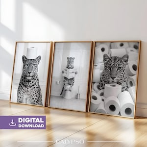 May include: Set of three framed black and white art prints featuring leopards. One leopard is wearing a roll of toilet paper, another is reading a newspaper on a toilet, and the third is surrounded by toilet paper rolls. The prints have gold frames.