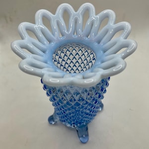 May include: A blue and white glass vase with a scalloped top and a diamond pattern. The vase has three legs and is made of clear glass.