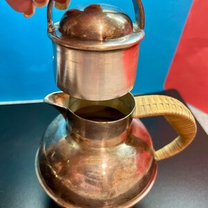 May include: A silver pitcher with a wicker handle and a silver lid. The lid has a small handle on top.