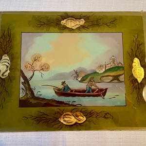 May include: A vintage framed landscape painting featuring a lake scene with two figures in a rowboat. The painting has a green border with gold-colored decorative accents. The artwork depicts a castle on a hill and a tree.