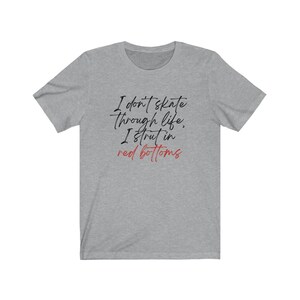 以下が含まれることがあります： ヘザーグレーのTシャツに「I don't skate through life, I strut in red bottoms」というテキストが黒と赤でプリントされています。