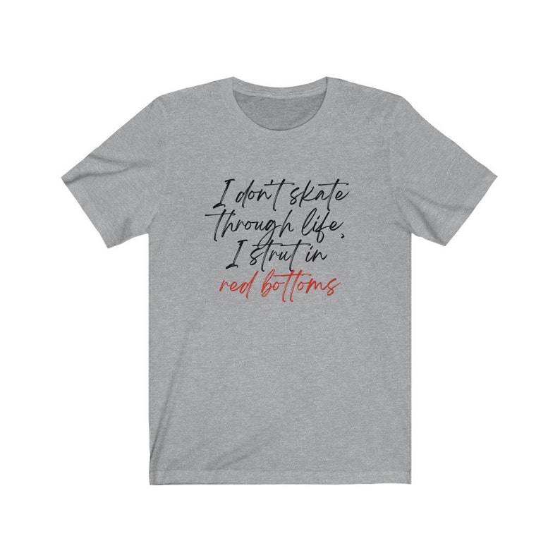 以下が含まれることがあります： ヘザーグレーのTシャツに「I don't skate through life, I strut in red bottoms」というテキストが黒と赤でプリントされています。
