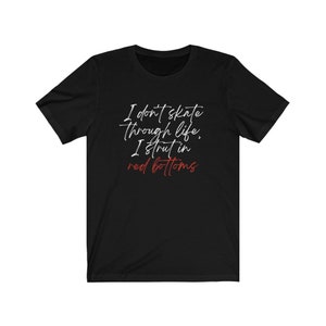 以下が含まれることがあります： 黒いTシャツに白い文字で「人生をスケートすることはない、赤い靴で歩くんだ」と書かれている。