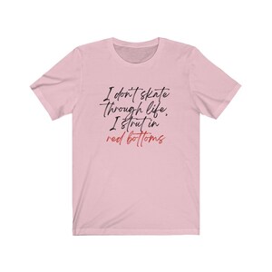 以下が含まれることがあります： ピンクのTシャツに「I don't skate through life, I strut in red bottoms」という黒い文字と赤い文字で書かれたテキストがプリントされています。