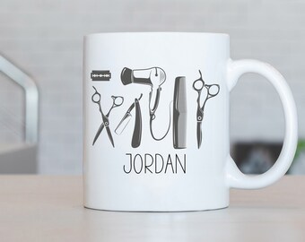 Peut inclure: Une tasse en céramique blanche avec un motif noir et blanc d'outils de coiffure, notamment des ciseaux, un rasoir, un peigne et un sèche-cheveux. Le texte "JORDAN" est imprimé sous le motif.