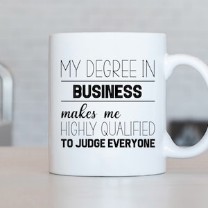 Może przedstawiać: Biały ceramiczny kubek do kawy z czarnym tekstem, który brzmi: "Mój dyplom z zarządzania sprawia, że ​​jestem wysoko wykwalifikowany, aby oceniać wszystkich."