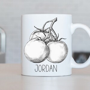 May include: White ceramic mug featuring a detailed black and white illustration of tomatoes on the vine. The name "JORDAN" is printed in a simple font below the illustration. The mug has a curved handle.