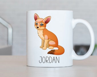 May include: White ceramic mug with a cartoon image of a fennec fox with orange fur and large ears. The mug has a black handle and the name "JORDAN" printed in black below the image.