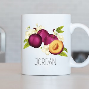 May include: White ceramic mug with a design of plums and white flowers. The mug has the name "JORDAN" printed on the front.