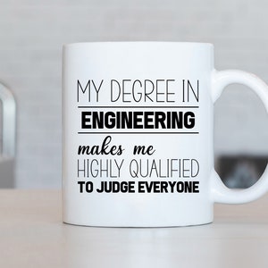 Peut inclure: Une tasse en céramique blanche avec du texte noir qui dit "Mon diplôme en ingénierie me rend hautement qualifié pour juger tout le monde."