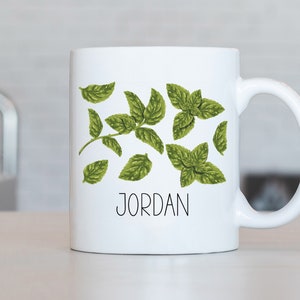 May include: White ceramic mug featuring a green leafy design and the name "JORDAN" printed in black.