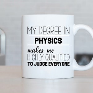 Può includere: Una tazza in ceramica bianca con testo nero che recita "La mia laurea in fisica mi rende altamente qualificato per giudicare tutti."